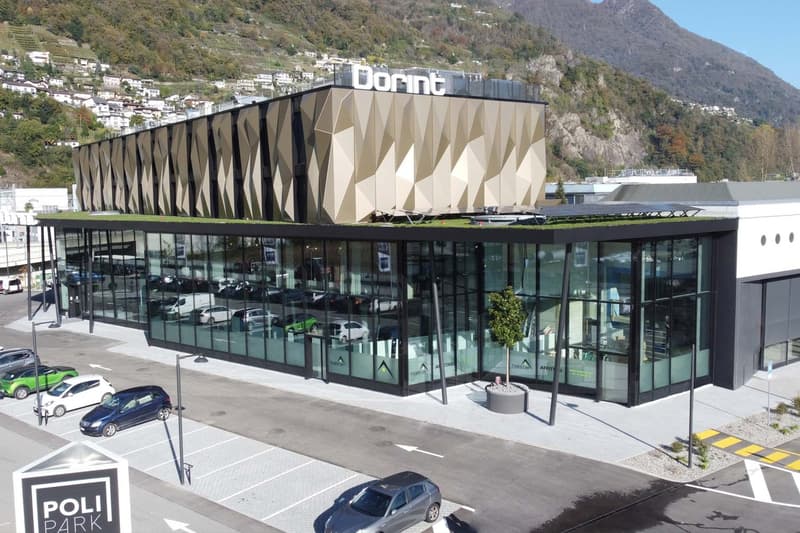 modern building, large glass windows, cars parked in front, mountain in the background