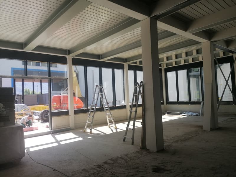 Interior of a building under construction, with large windows, metal beams, and ladders.