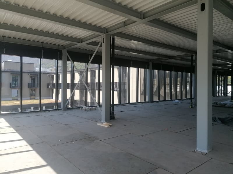 Empty building interior with large glass windows, metal beams, and concrete floor.