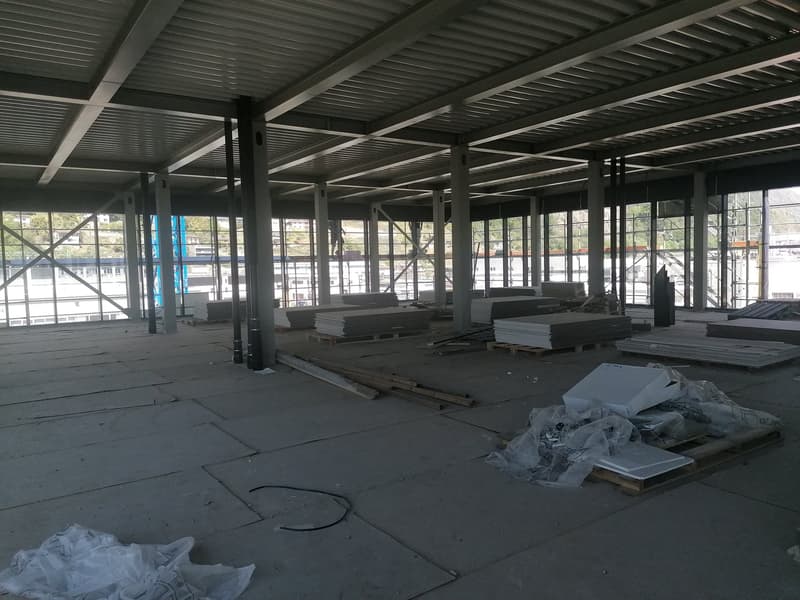 Empty building with large windows, metal beams, and construction materials