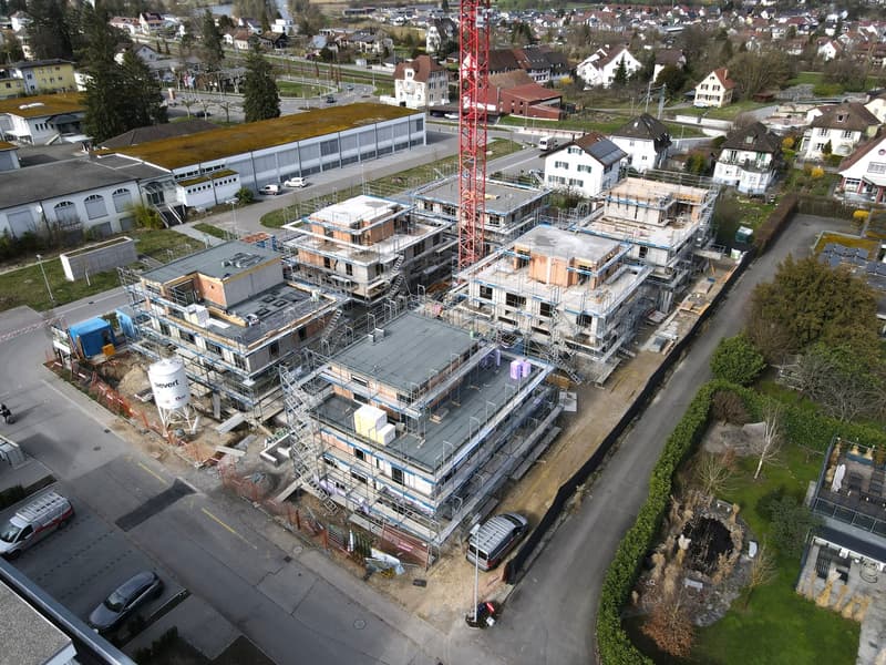 Aerial view of a construction site with multiple buildings under construction, surrounded by other buildings and greenery.