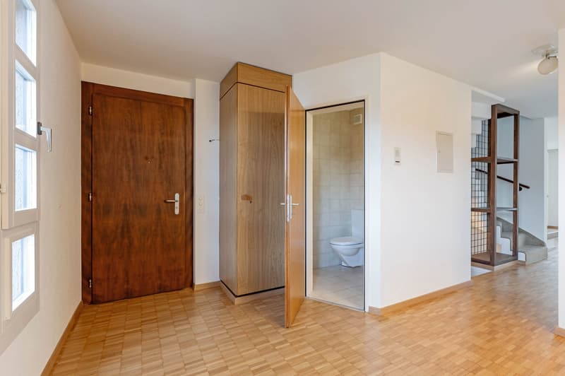 Empty room with wooden door, wooden cabinet, open door to bathroom, wooden floor, white walls