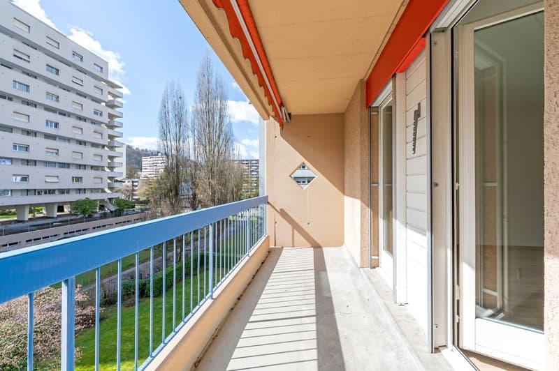 Balcony with blue railings, beige wall, white door, glass door, green grass, trees, buildings
