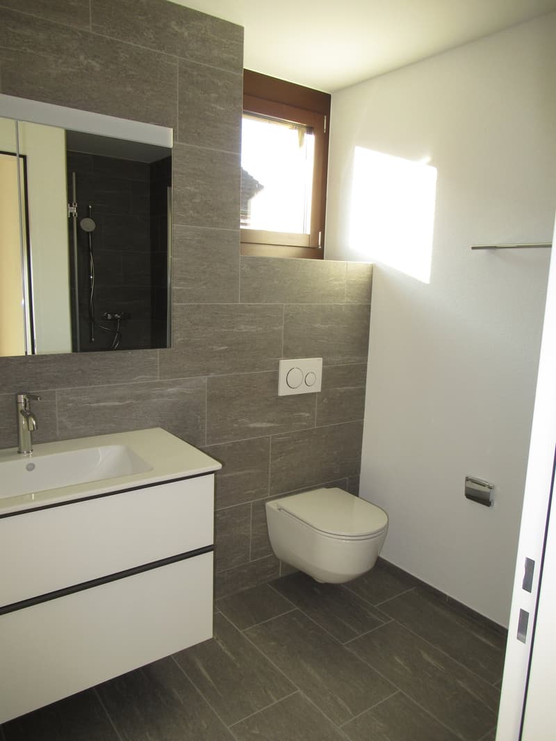 Bathroom with white sink, mirror, and toilet, gray tiles, white walls, small window