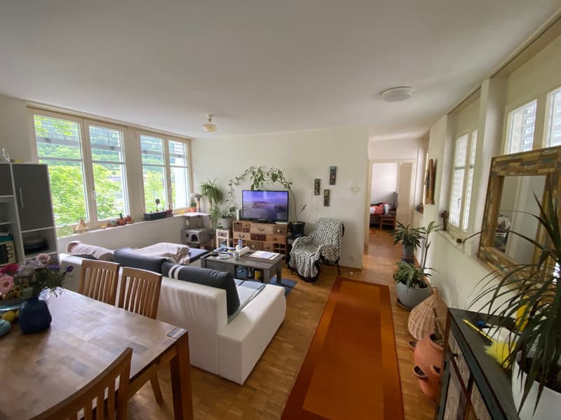 living room with white couch, wooden table, TV, plants, wooden floor, large windows