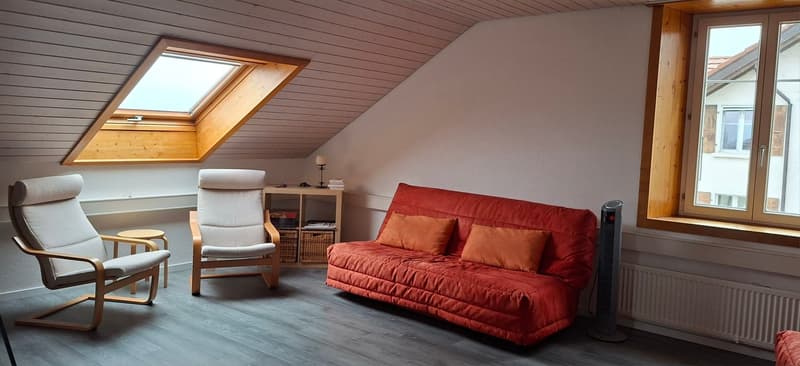 small attic room with sofa, two chairs, table, radiator and skylight