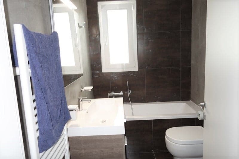 small, brown tiles, white bathtub, white toilet, white sink, blue towel, small shower, white door
