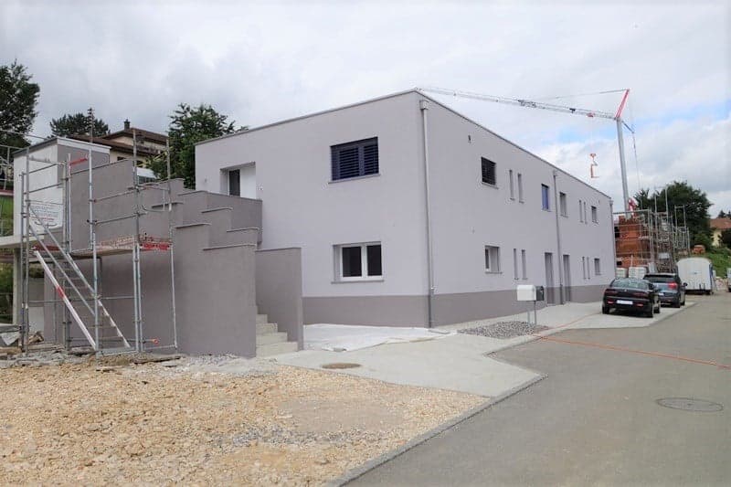 New building, modern design, under construction, concrete exterior, few windows, cars parked in front, crane visible