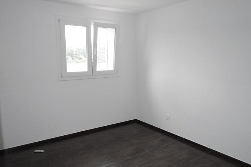 An empty room with white walls, tiled floor, a window with white frames, and an electrical outlet.