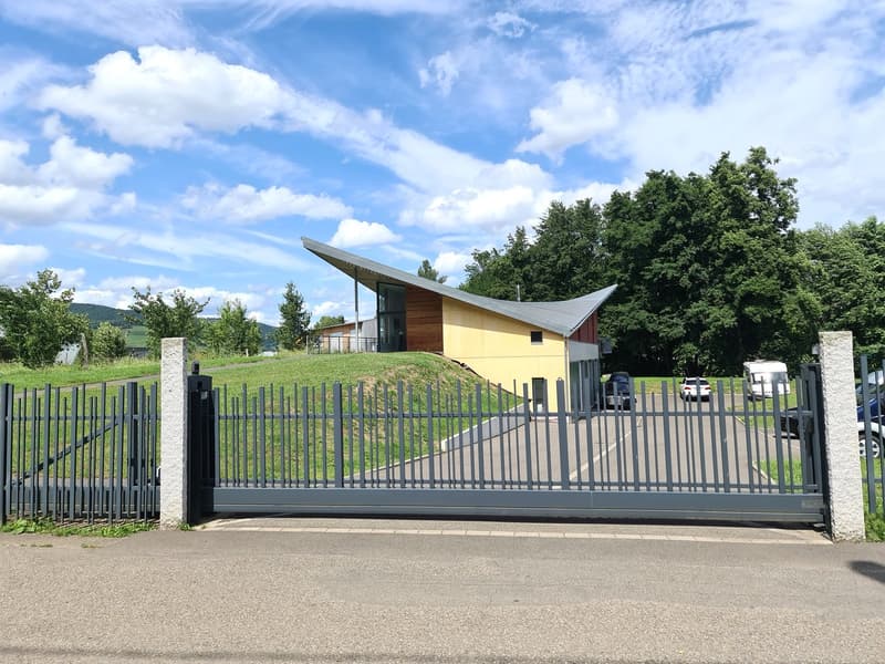 contemporary design house, yellow exterior, sloping roof, multiple windows, enclosed by a fence, car parked in front