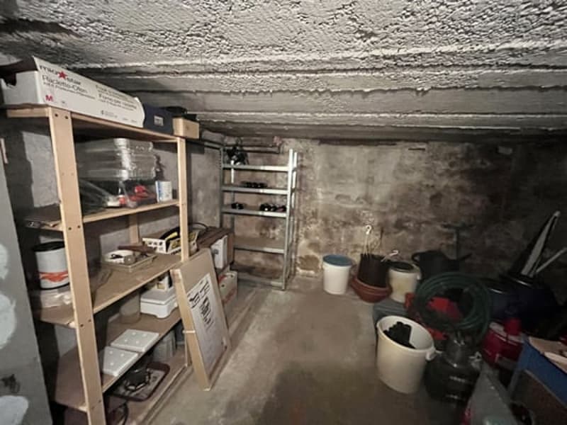Unfinished basement with concrete walls and floor, shelving units for storage, various household items and tools scattered around