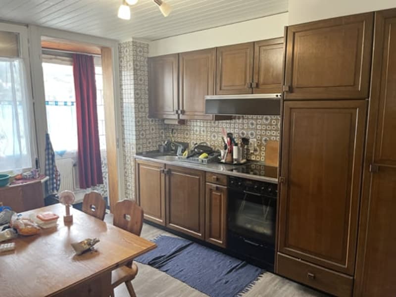 The image shows a kitchen with wooden cabinets, a tile backsplash, and a dining table with chairs. There is a dishwasher visible in the kitchen.