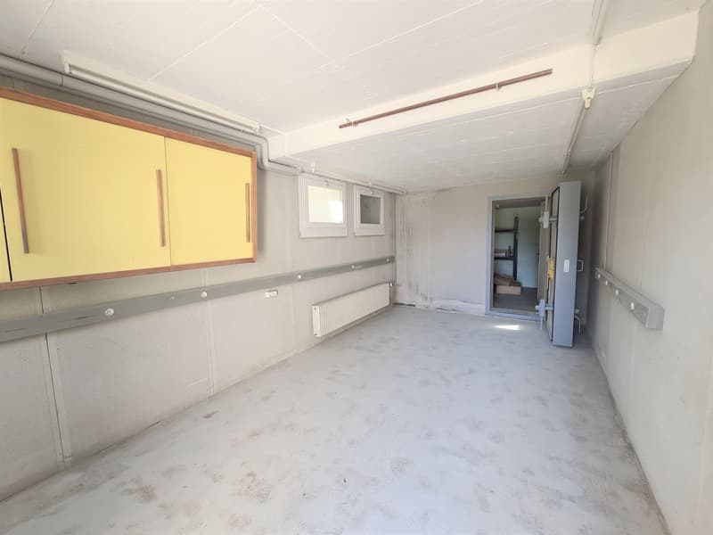 This image shows a large, open room with white walls and a concrete floor. The room has built-in cabinets and shelves along one wall, with a yellow and wood-tone color scheme. There is a window visible, and the room appears to be in a state of renovation