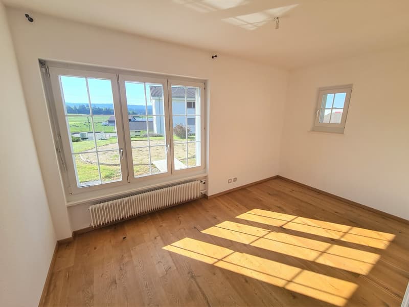 Spacious bedroom with large windows offering a scenic view of the surrounding countryside. The room features hardwood flooring and is filled with natural light.