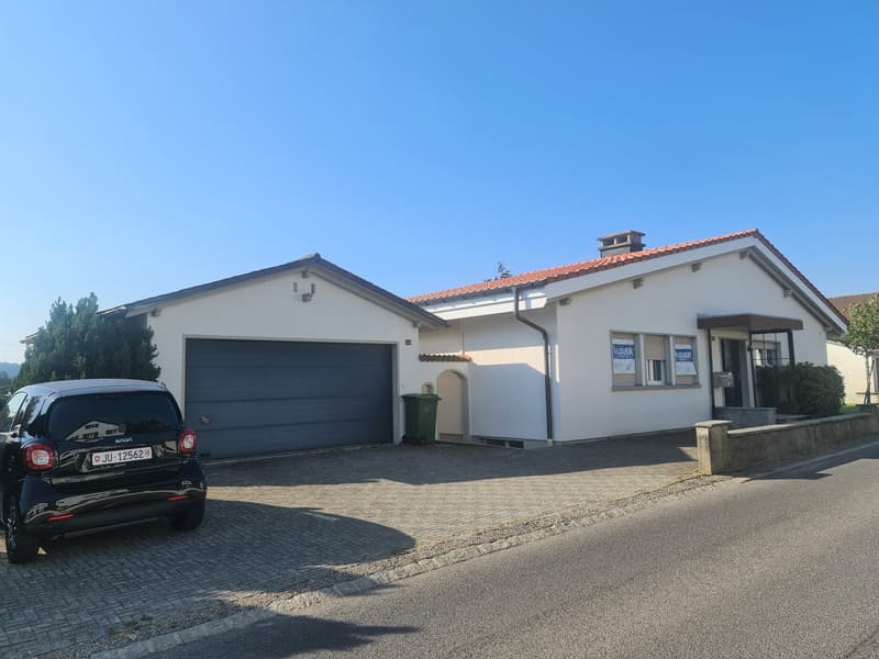 Single-story house with a garage, white exterior walls, red tile roof, and a paved driveway with a parked car