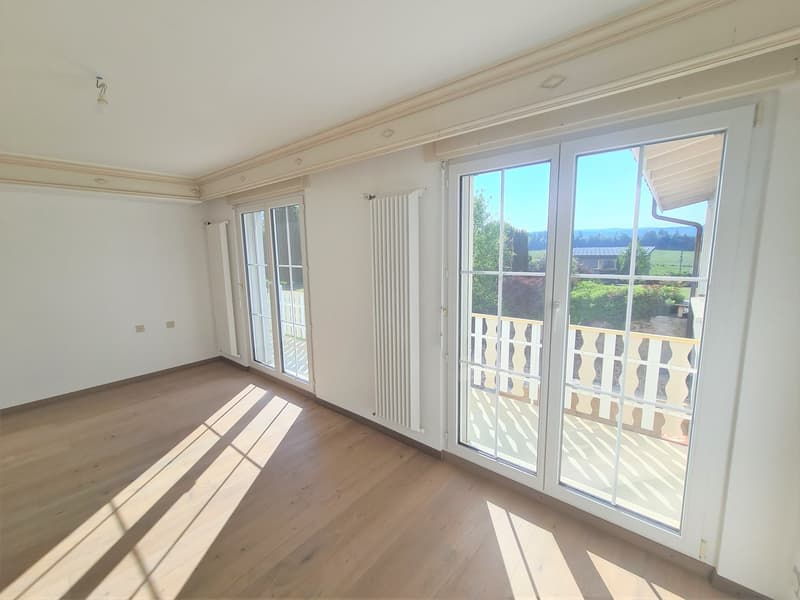 Spacious living room with large windows, hardwood floors, and access to a balcony or terrace overlooking the surrounding landscape.