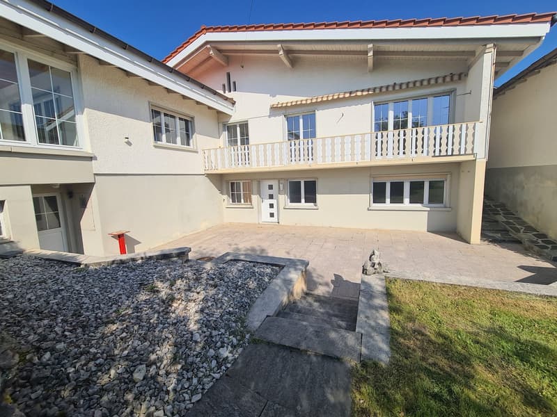 2-story house with stucco exterior, red tile roof, balcony on the second floor, paved driveway, and landscaped yard with gravel and grass.