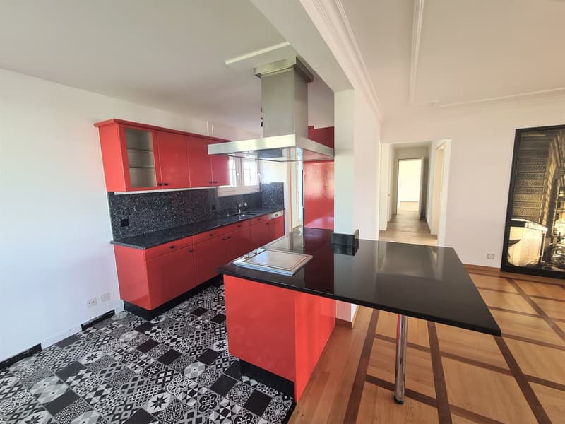 Modern kitchen with red cabinets, black granite countertops, patterned tile flooring, and a stainless steel range hood.