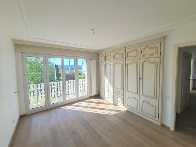 Spacious bedroom with large windows overlooking a balcony, hardwood flooring, and built-in wardrobes along the wall.