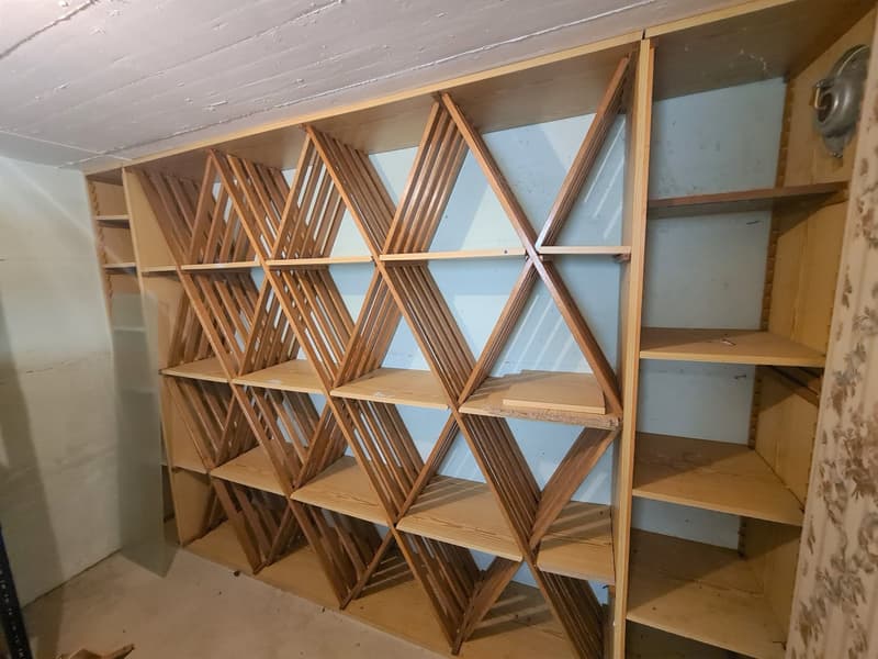 The image shows a wooden shelving unit with a triangular geometric pattern. The shelves are made of wooden slats arranged in a criss-cross pattern, creating a visually interesting and functional storage solution.