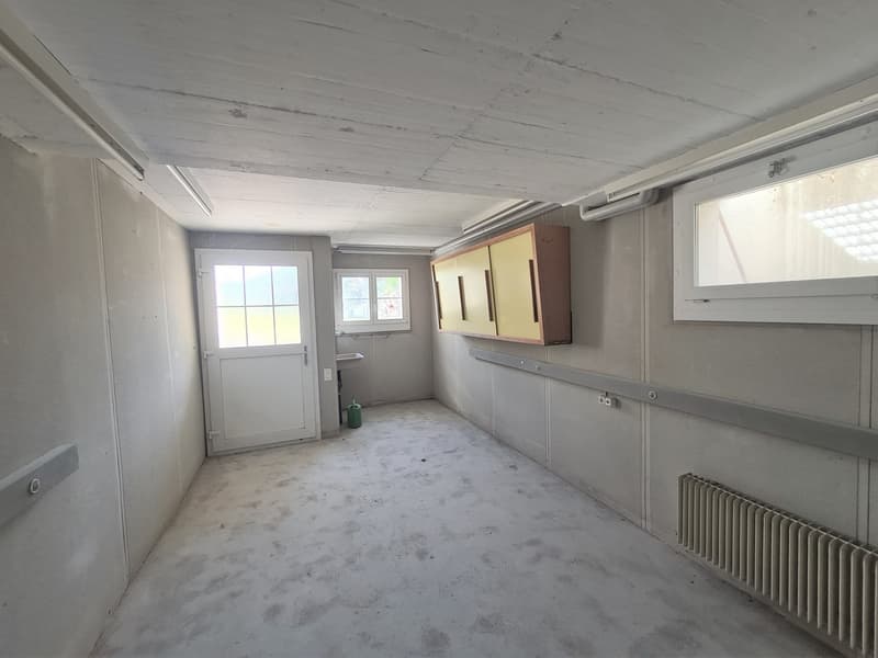 This image shows an empty room with a concrete floor, white walls, and a window. The room appears to be in a state of renovation or construction, with some built-in cabinets or shelving units visible along the walls.