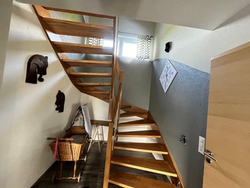 Wooden staircase with metal railing leading to an upper level, with decorative elephant figurines on the wall and a basket on the landing.