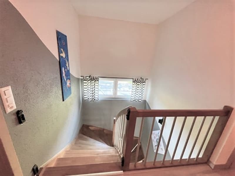 Wooden staircase with railing, leading to an upper level. The walls are painted in a light color, and there is a decorative wall art piece visible.