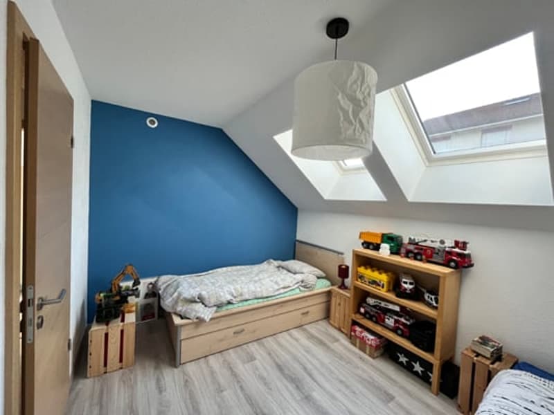 Attic bedroom with slanted ceiling, blue accent wall, wooden bed frame, shelving unit, and skylights