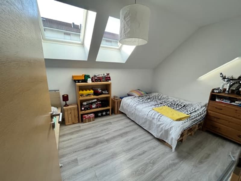 Bedroom with hardwood-style flooring, white walls, large window, shelving unit, dresser, and bed with gray bedding