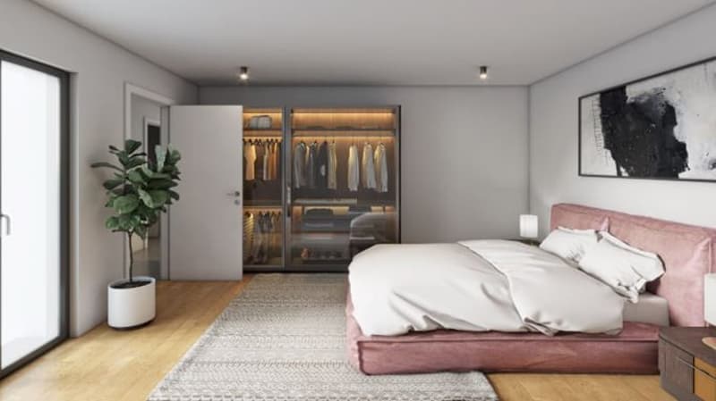 modern bedroom with white walls, wooden floor, walk-in closet with full-length mirrors, a bed with pink headboard, area rug, and a potted plant.