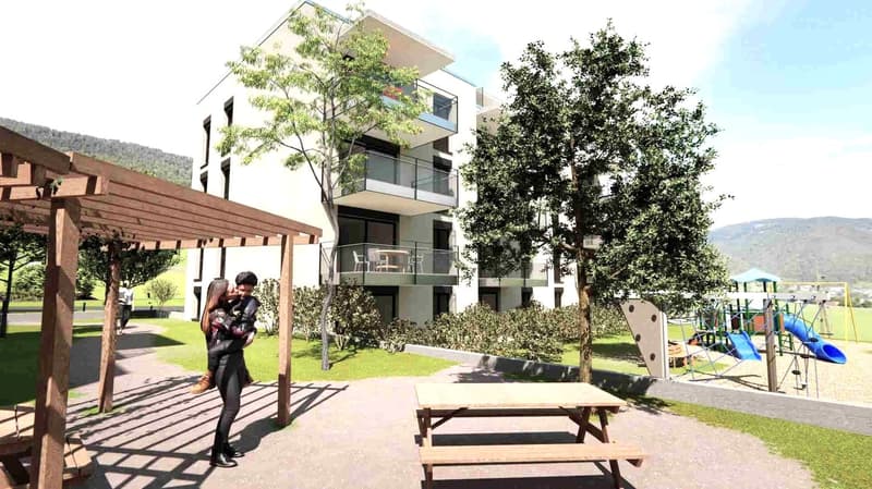 Modern apartment building with multiple balconies, a well-maintained outdoor area with grassy lawns, a wooden pergola, and a wooden picnic table. An outdoor playground with a slide and swings is also visible.