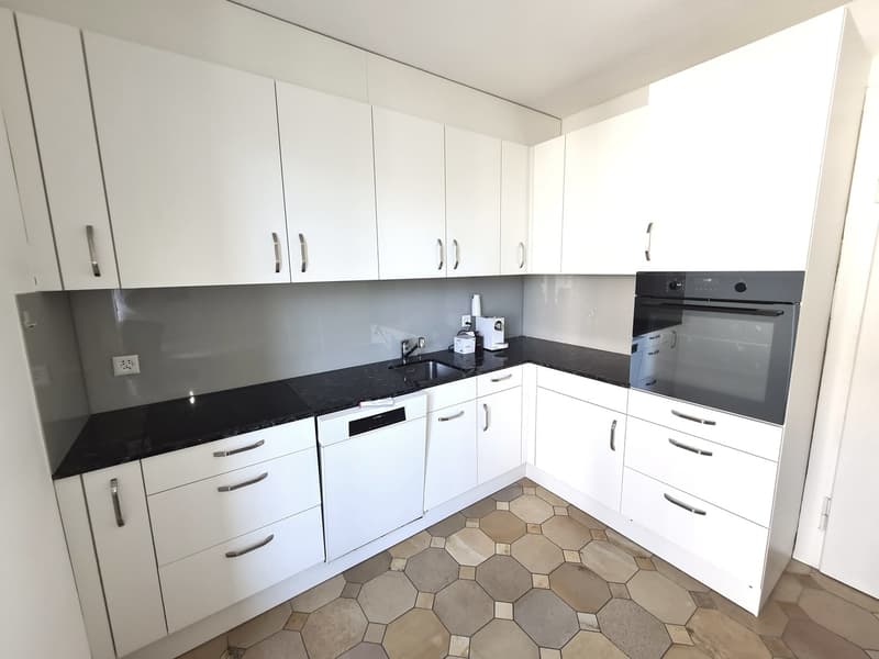 Modern kitchen with white cabinets, black countertops, built-in oven, and hexagonal tile flooring