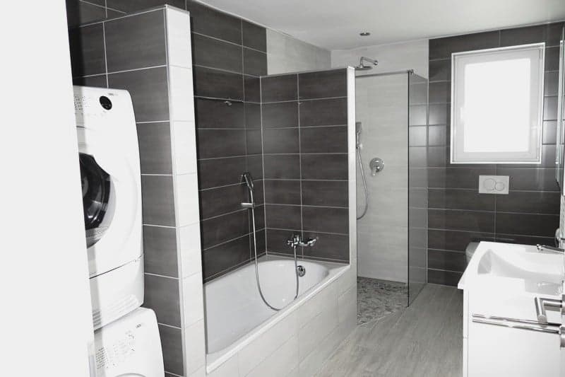 Large bathroom with dark gray tile walls, bathtub, shower, and a washing machine