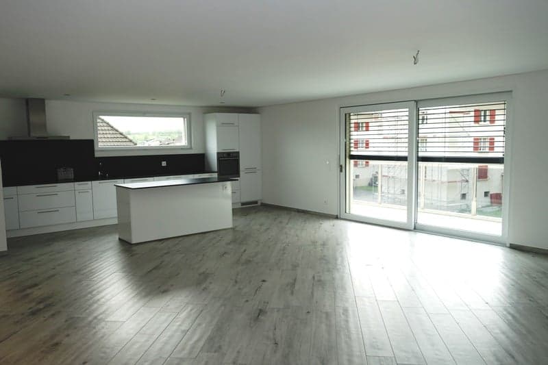 Open-concept living space with a modern kitchen, large windows, and hardwood flooring throughout.