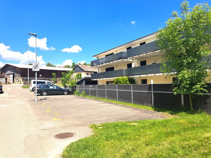 3-story apartment building with balconies, surrounded by trees and greenery, parking lot in front
