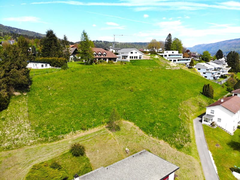 Building plot with green meadow, mountains in the background, several houses in the background