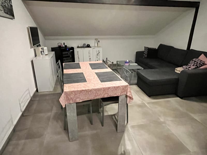 an attic room with a dining table, chairs, a table, a black sofa, a cabinet, a television