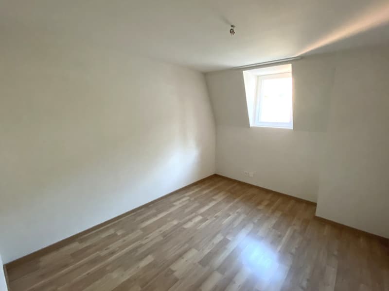 Empty room, wooden floor, white walls, single window.
