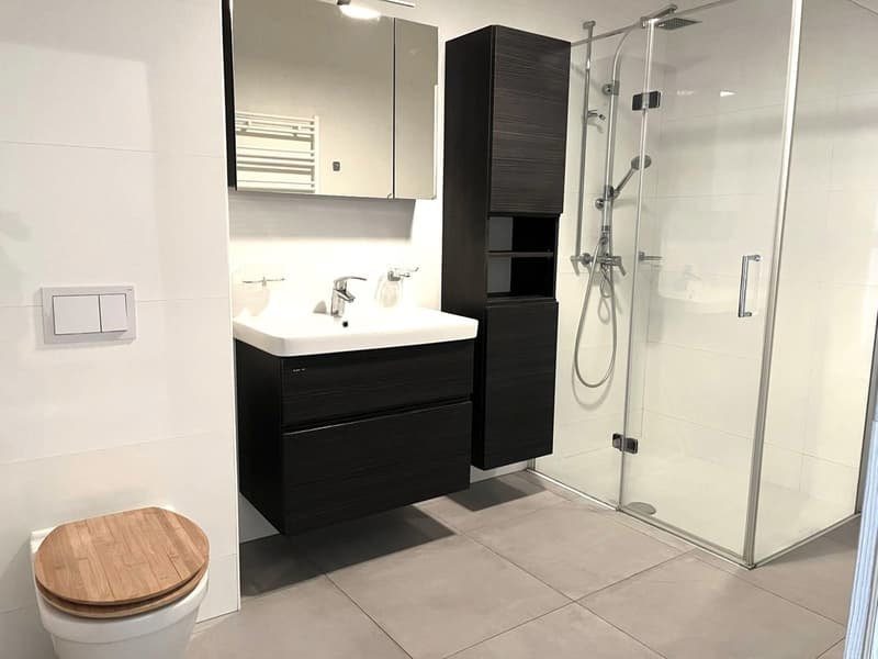 modern bathroom with wooden toilet seat, white sink, black cabinets, glass shower, mirror, and chrome shower head