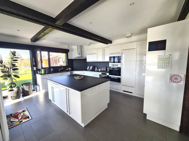 White modern kitchen with black island countertop, white cupboards, black accents, large window with sliding doors, white walls, modern appliances.