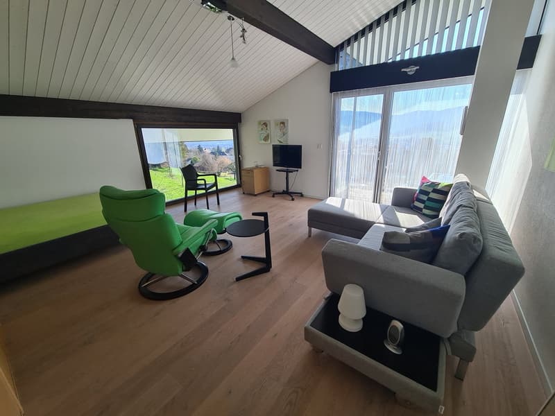 Modern loft living room with gray couch, green reclining chair, black side table, TV, panoramic window, wooden floor