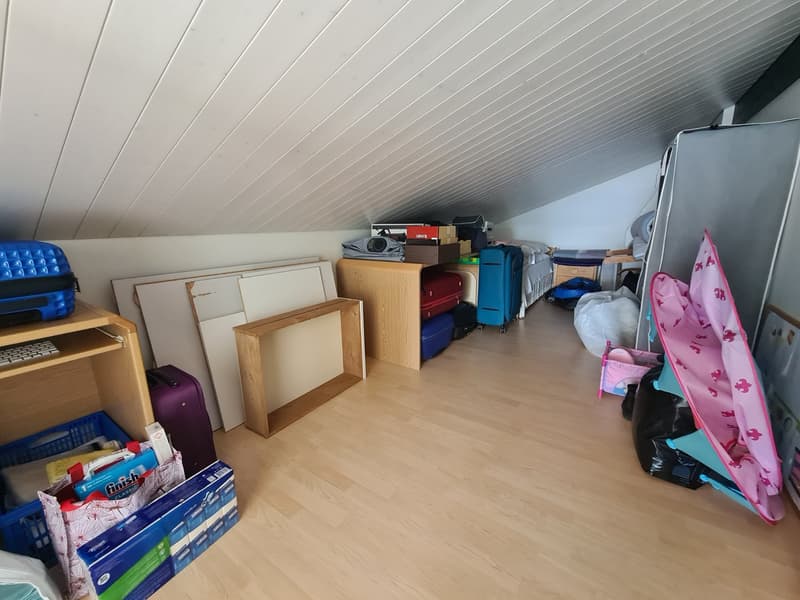 attic, wooden flooring, white ceiling, with various objects, including luggage, boxes, and a whiteboard