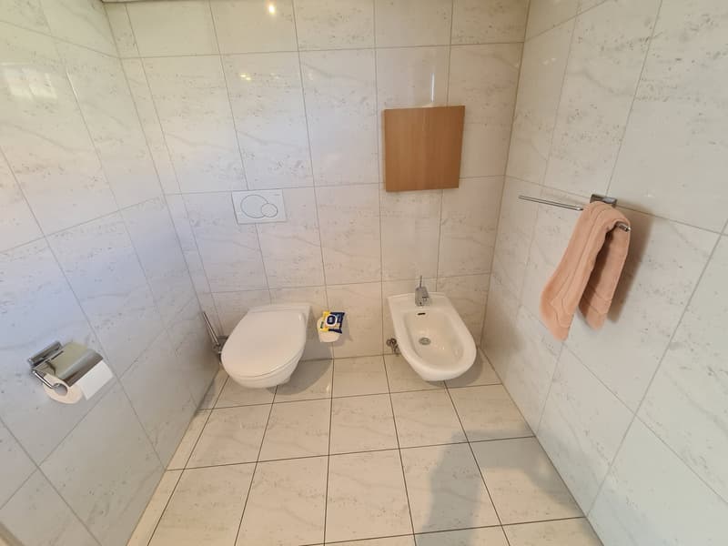 Compact bathroom with white tiles, modern toilet, bidet, and towel rack