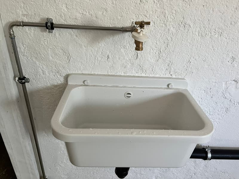 The image shows a white utility sink mounted on the wall, with a metal faucet and pipe fixture attached to it.