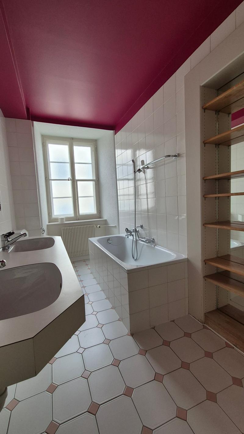 Modern bathroom with white hexagonal tiles, a burgundy ceiling, a bathtub, double sink, and open shelving.