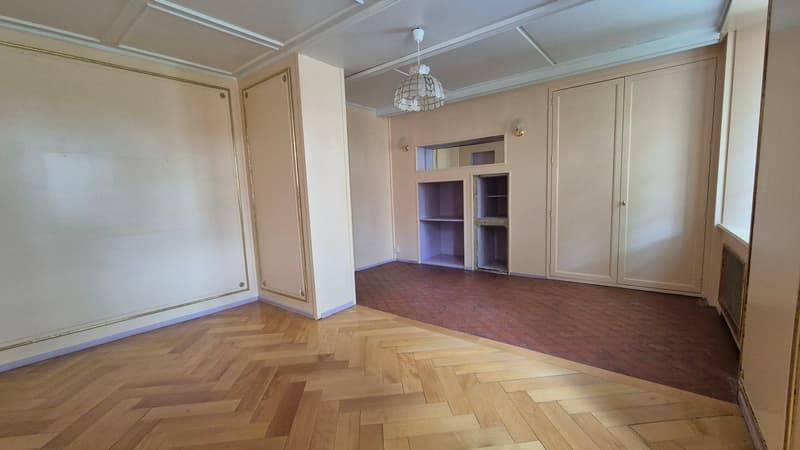Empty room, wooden parquet flooring, two types of flooring, large open closets, beige walls, hanging ceiling lamp, sconces, large window on the wall