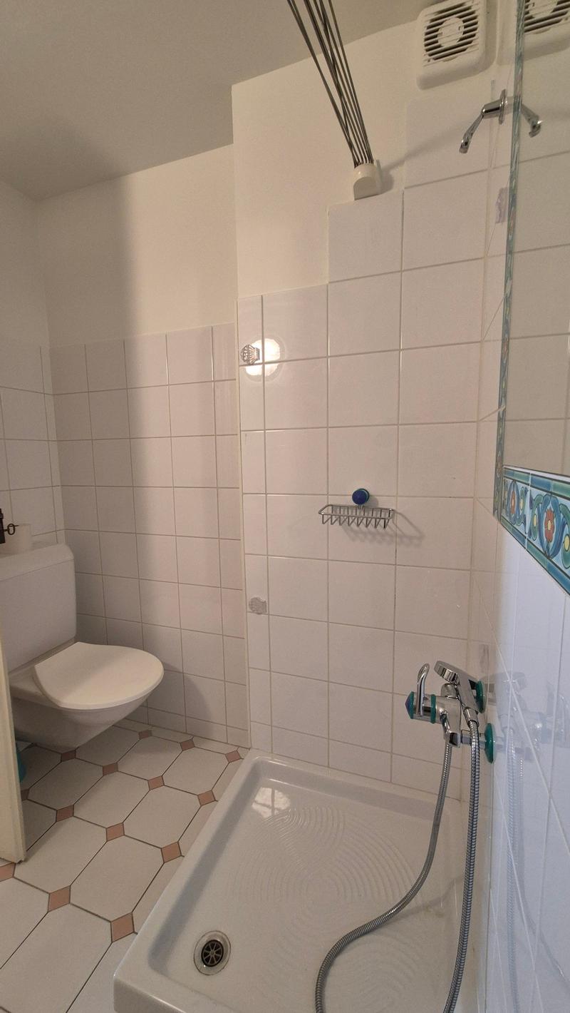 Tiled walls and floor, a white toilet, a bathtub with a shower head, a towel rack, and a ventilation unit