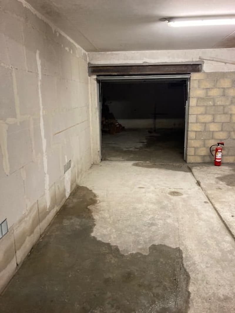 Empty garage, open door, concrete floor, fire extinguisher on the right side, brick wall, white painted wall