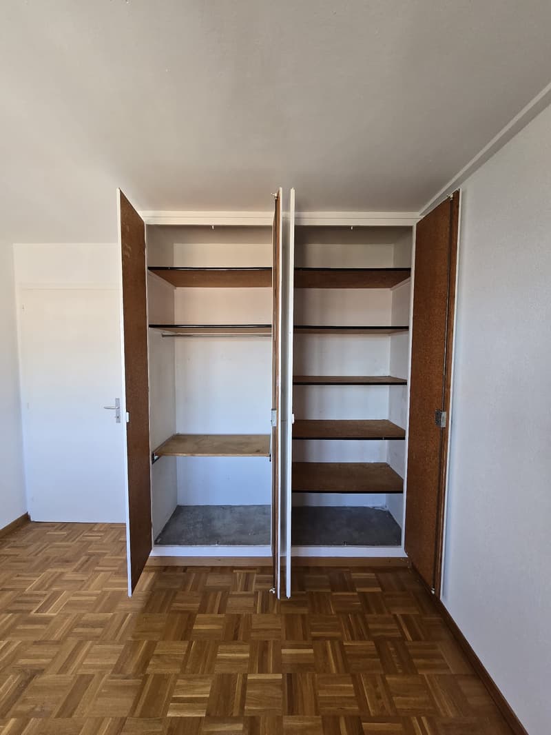 Empty wardrobe with doors open, wooden floors, white walls