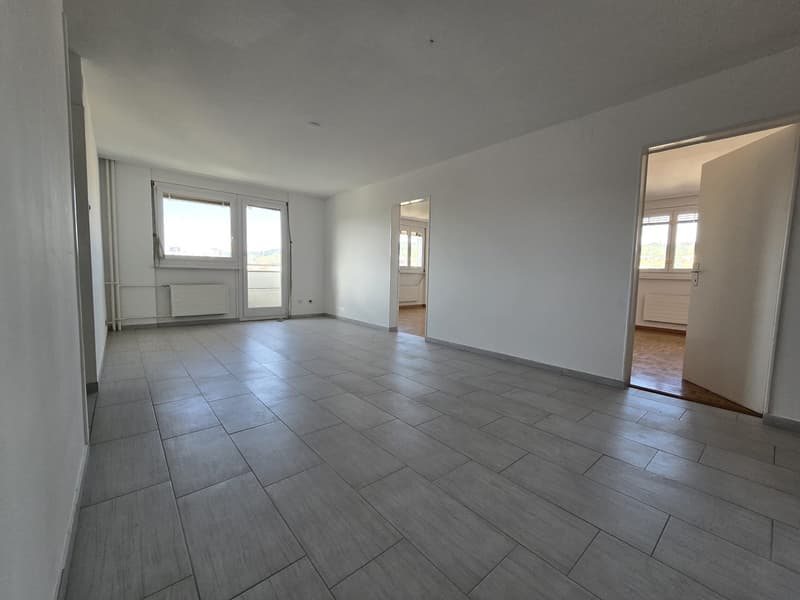 empty room, gray tile flooring, white walls, two doors leading to other rooms, large windows with views outside, radiators